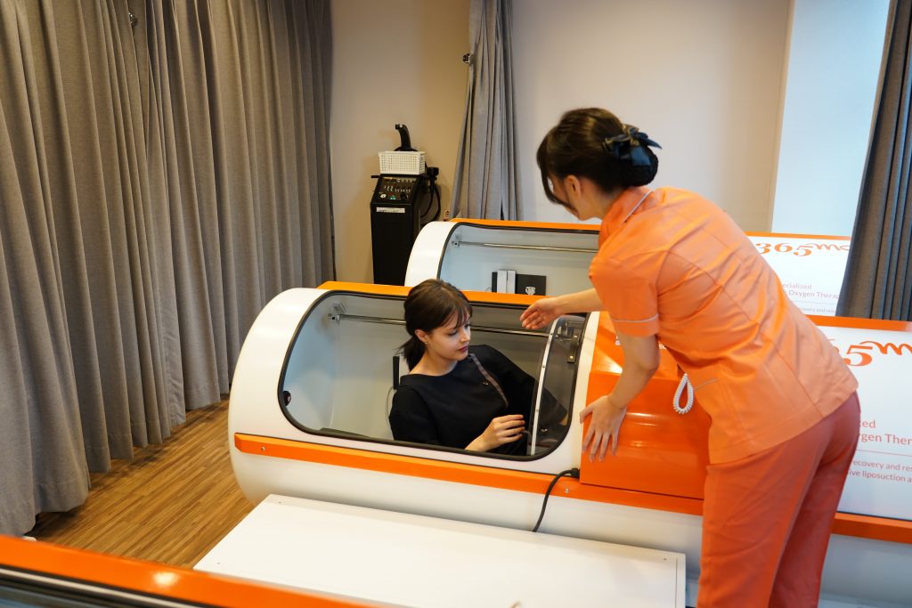 Nurse assisting patient into hyperbaric oxygen tube at 365mc for post-liposuction recovery